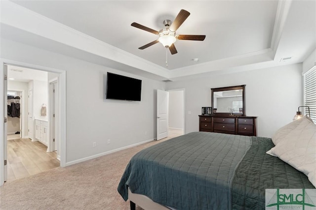 carpeted bedroom with ceiling fan, ensuite bath, a tray ceiling, and crown molding