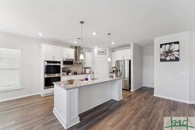 kitchen with wall chimney exhaust hood, white cabinetry, stainless steel appliances, hanging light fixtures, and a center island with sink