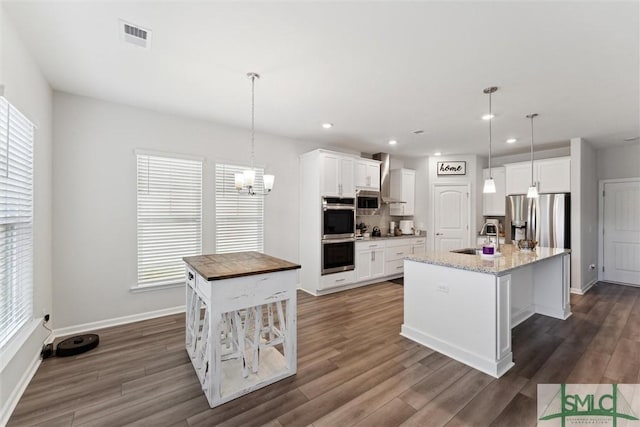 kitchen with decorative light fixtures, white cabinets, appliances with stainless steel finishes, and a center island with sink