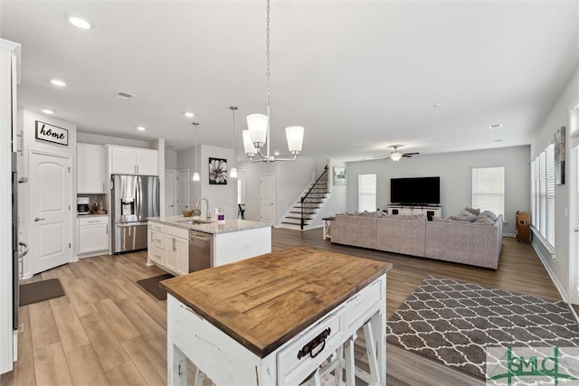 kitchen with sink, a kitchen island with sink, appliances with stainless steel finishes, white cabinets, and light stone counters