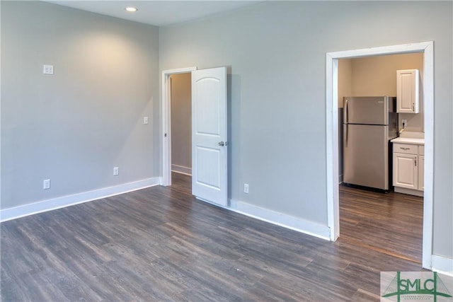 unfurnished bedroom featuring stainless steel fridge, connected bathroom, and dark hardwood / wood-style floors