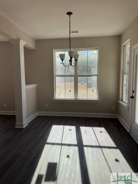 unfurnished dining area with dark wood-type flooring, an inviting chandelier, and a healthy amount of sunlight