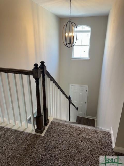 stairway featuring carpet floors, baseboards, and a notable chandelier