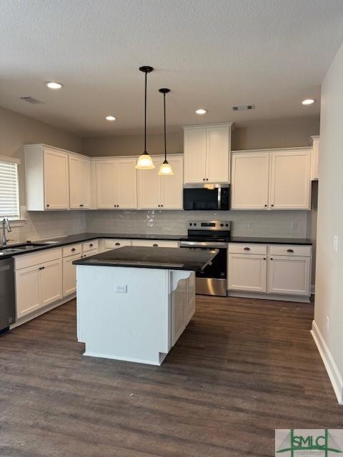 kitchen with stainless steel appliances, a sink, white cabinetry, dark countertops, and decorative light fixtures