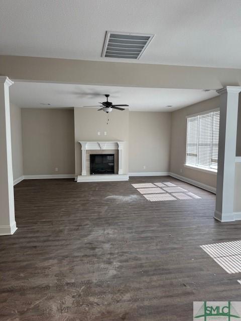 unfurnished living room with ceiling fan, a fireplace, visible vents, and dark wood-style flooring