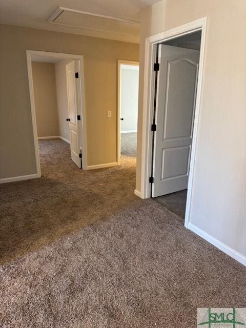 empty room with attic access, dark colored carpet, and baseboards