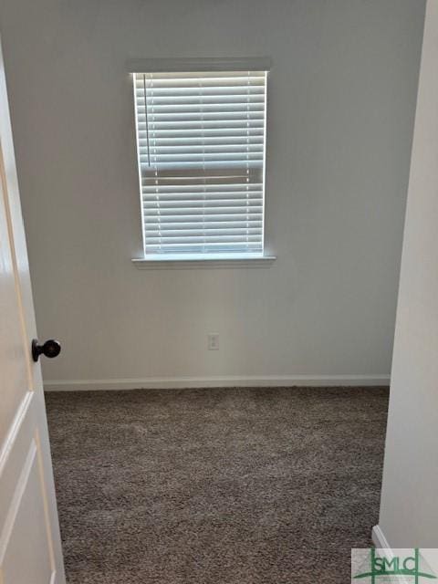 unfurnished room featuring dark carpet and baseboards