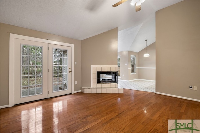 unfurnished living room with ceiling fan, vaulted ceiling, a tiled fireplace, and light hardwood / wood-style flooring