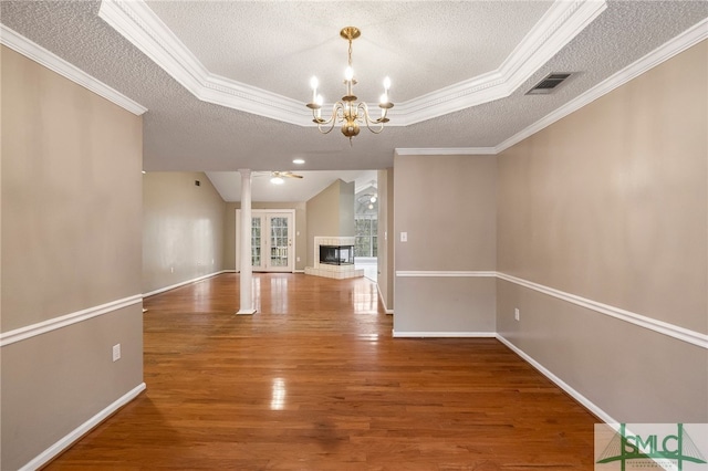 unfurnished living room with ceiling fan with notable chandelier, a textured ceiling, a fireplace, ornamental molding, and hardwood / wood-style flooring