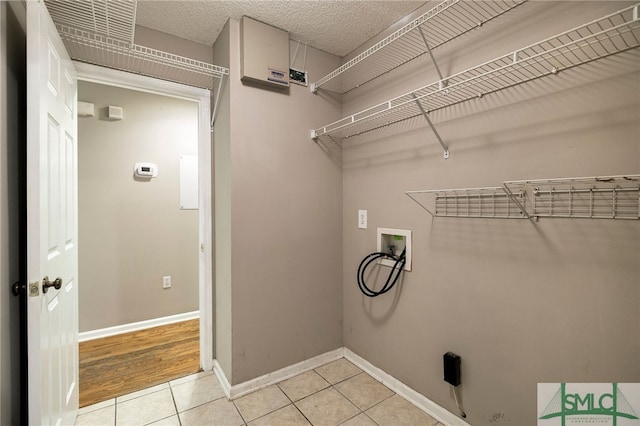 clothes washing area with light tile patterned flooring, hookup for a washing machine, and a textured ceiling