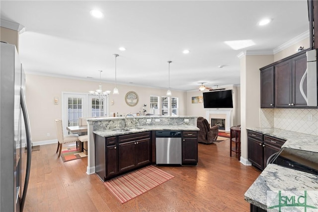 kitchen with pendant lighting, appliances with stainless steel finishes, dark brown cabinets, light stone countertops, and an island with sink