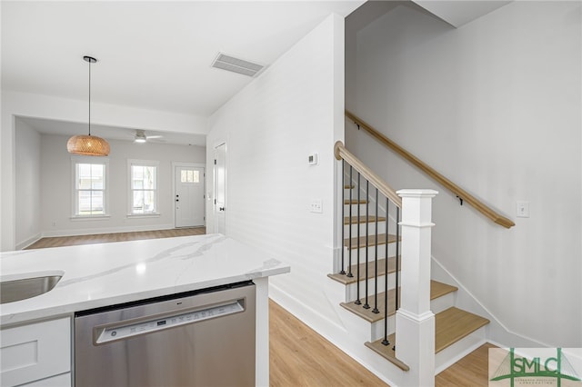 kitchen with light wood-type flooring, stainless steel dishwasher, light stone counters, and decorative light fixtures