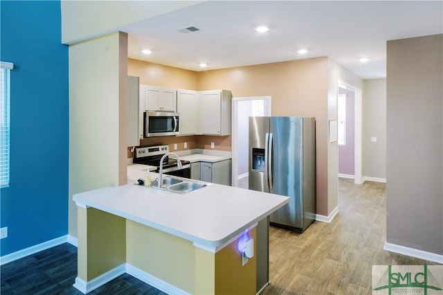 kitchen with white cabinets, appliances with stainless steel finishes, sink, kitchen peninsula, and light wood-type flooring