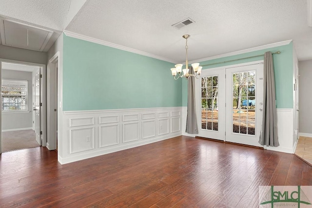 unfurnished dining area featuring a textured ceiling, dark hardwood / wood-style flooring, ornamental molding, and a notable chandelier