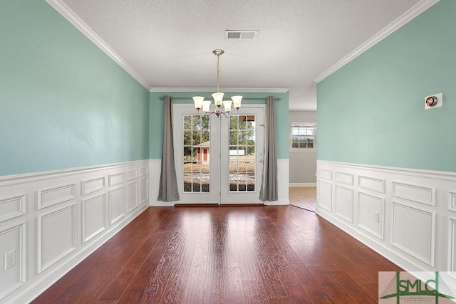 unfurnished dining area with a textured ceiling, dark hardwood / wood-style floors, crown molding, and an inviting chandelier