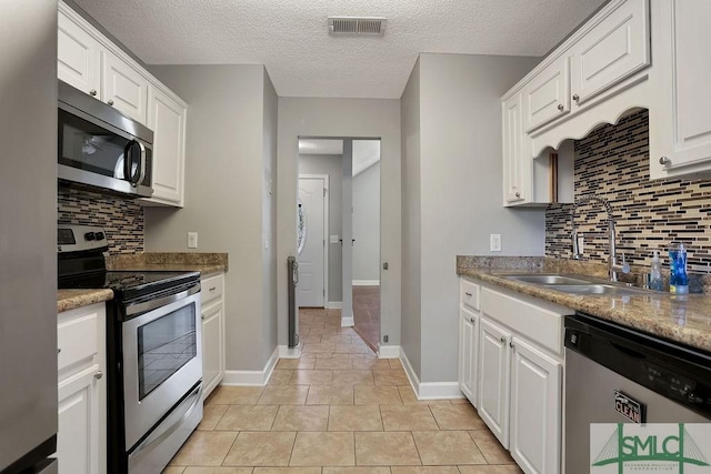 kitchen with light tile patterned floors, stainless steel appliances, backsplash, and white cabinetry