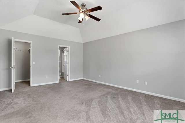 unfurnished bedroom featuring a spacious closet, ceiling fan, a closet, vaulted ceiling, and carpet flooring