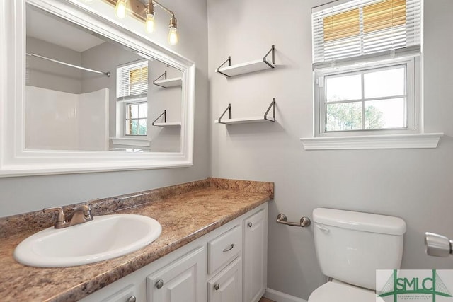 bathroom with toilet, a healthy amount of sunlight, vanity, and walk in shower