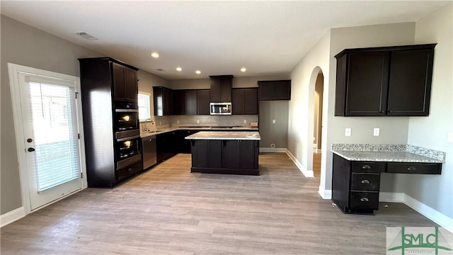 kitchen with appliances with stainless steel finishes, a kitchen island, light hardwood / wood-style floors, sink, and backsplash