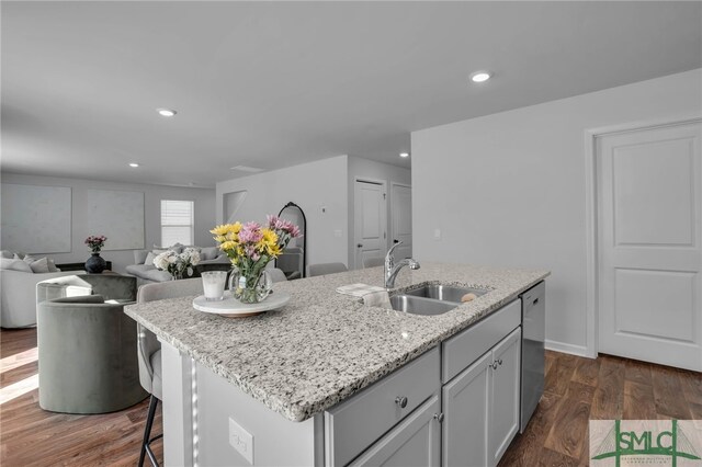 kitchen featuring dishwasher, sink, dark hardwood / wood-style floors, a kitchen island with sink, and light stone counters