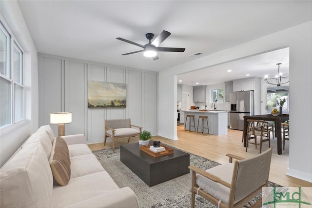 living room featuring sink, ceiling fan with notable chandelier, and light hardwood / wood-style floors