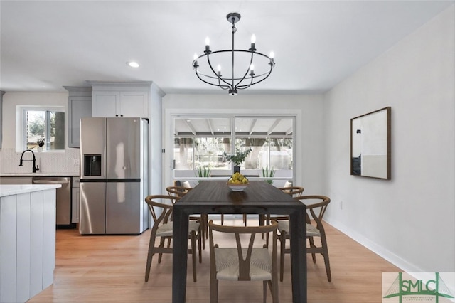 dining space with light wood-type flooring, sink, and an inviting chandelier