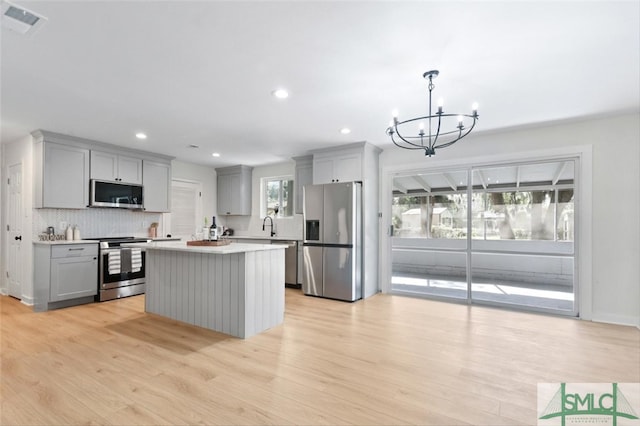 kitchen featuring decorative light fixtures, stainless steel appliances, a notable chandelier, light wood-type flooring, and gray cabinetry