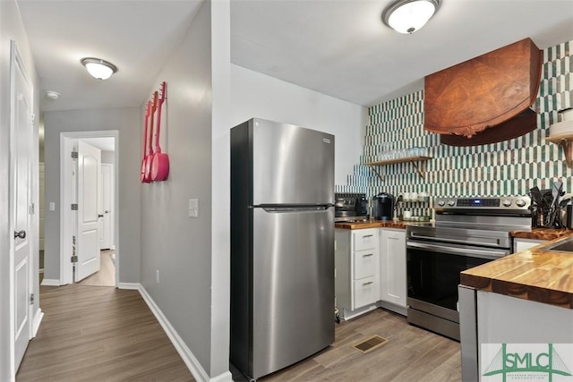 kitchen featuring white cabinets, appliances with stainless steel finishes, wood counters, wood-type flooring, and backsplash