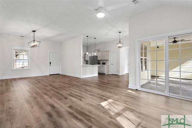 unfurnished living room with lofted ceiling, ceiling fan with notable chandelier, and hardwood / wood-style floors