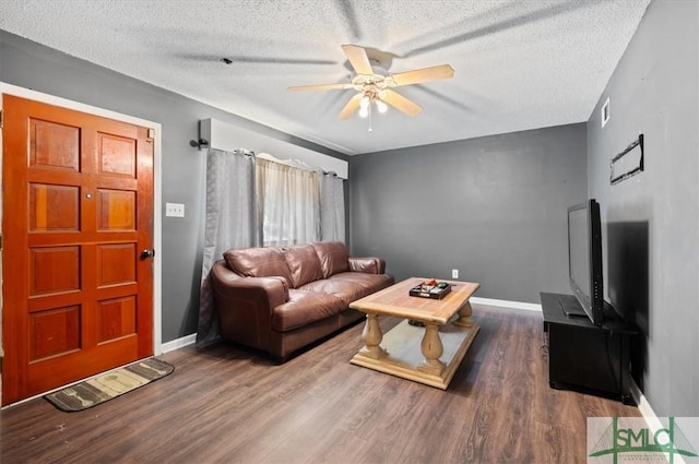 living room with a textured ceiling, ceiling fan, and dark wood-type flooring