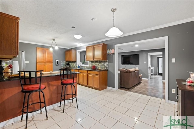 kitchen featuring backsplash, pendant lighting, crown molding, a kitchen breakfast bar, and light tile patterned floors