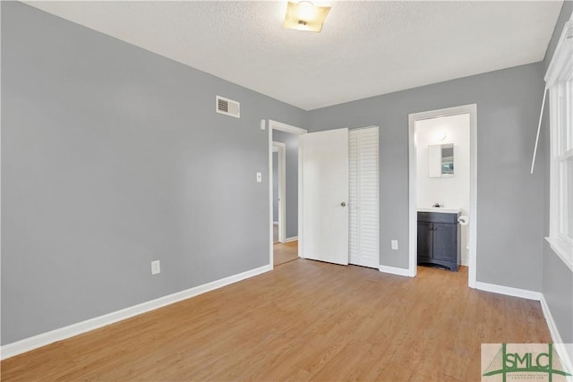 unfurnished bedroom with a textured ceiling, a closet, ensuite bathroom, and light hardwood / wood-style floors