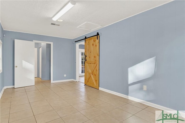 spare room featuring a barn door, light tile patterned floors, and a textured ceiling