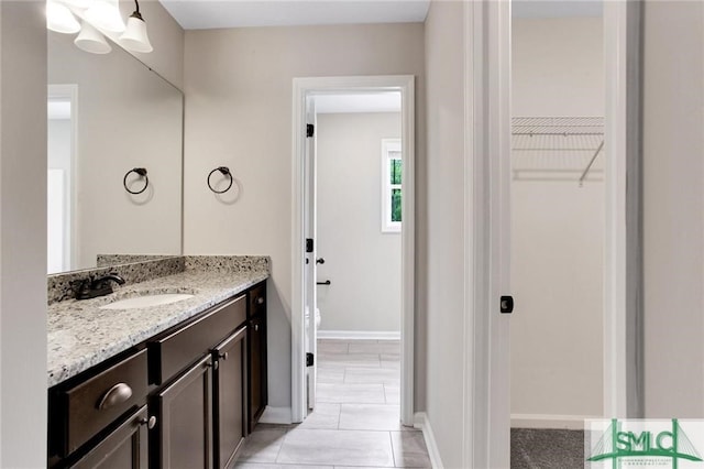 bathroom with toilet, a spacious closet, baseboards, and vanity