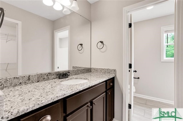 bathroom with toilet, a spacious closet, vanity, and baseboards