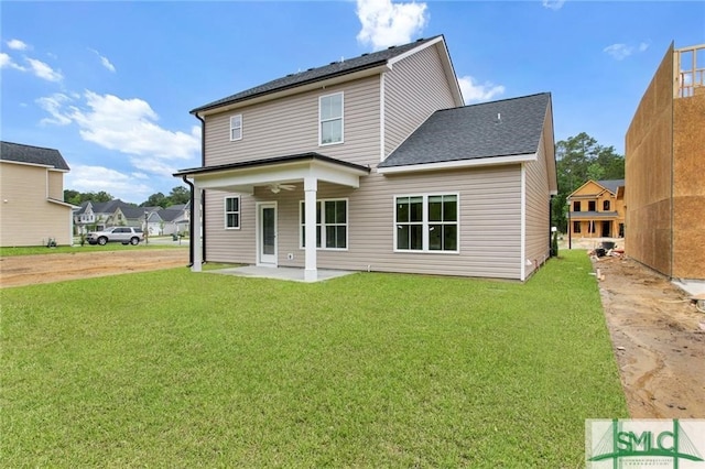 back of house featuring roof with shingles, a lawn, and a patio area