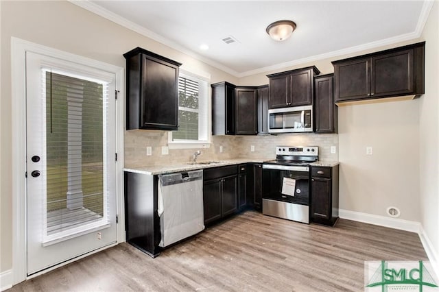 kitchen featuring stainless steel appliances, backsplash, ornamental molding, a sink, and light wood-type flooring