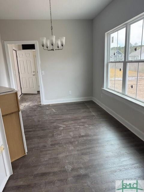 unfurnished dining area featuring baseboards, a chandelier, and dark wood-style flooring
