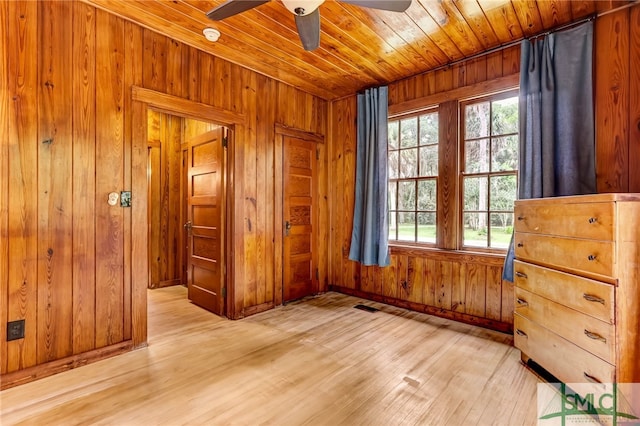 unfurnished bedroom with ceiling fan, wood ceiling, wooden walls, and light hardwood / wood-style floors