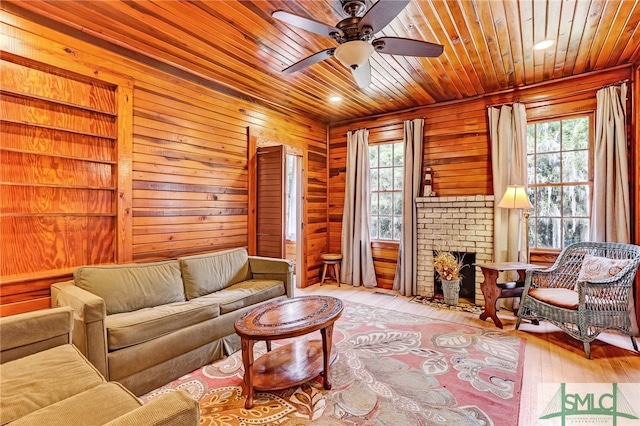 living room with ceiling fan, a brick fireplace, wood walls, light hardwood / wood-style flooring, and wood ceiling