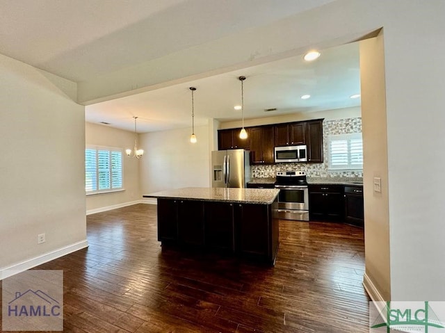 kitchen with appliances with stainless steel finishes, backsplash, hanging light fixtures, light stone countertops, and a kitchen island