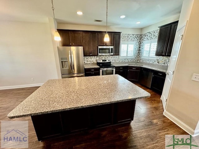 kitchen featuring light stone counters, hanging light fixtures, appliances with stainless steel finishes, and a center island