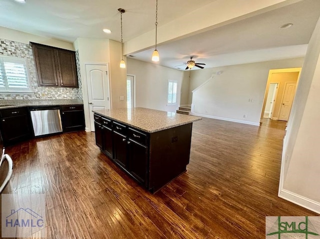 kitchen featuring ceiling fan, dishwasher, hanging light fixtures, light stone counters, and a center island