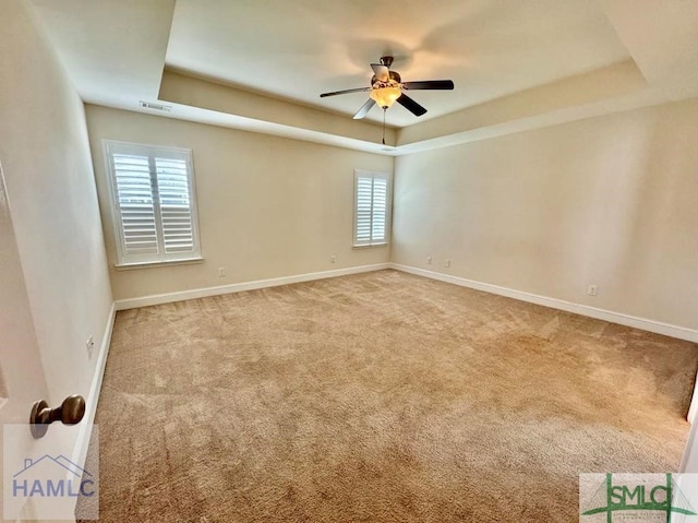 carpeted empty room with a raised ceiling, ceiling fan, and a wealth of natural light