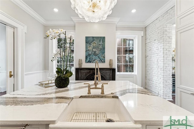 room details featuring light stone counters, ornamental molding, a kitchen island with sink, and sink