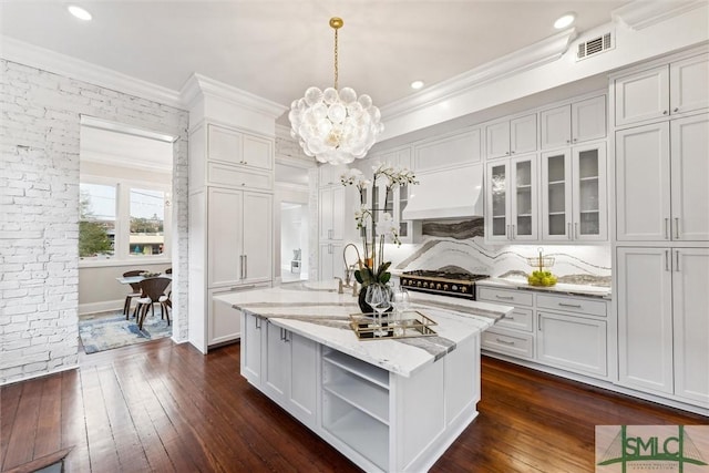 kitchen with range, dark hardwood / wood-style floors, light stone countertops, a center island with sink, and decorative light fixtures