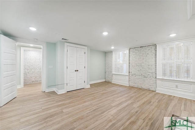 unfurnished bedroom with brick wall and light hardwood / wood-style floors