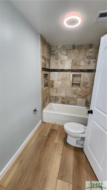 bathroom with wood-type flooring, toilet, and tiled shower / bath