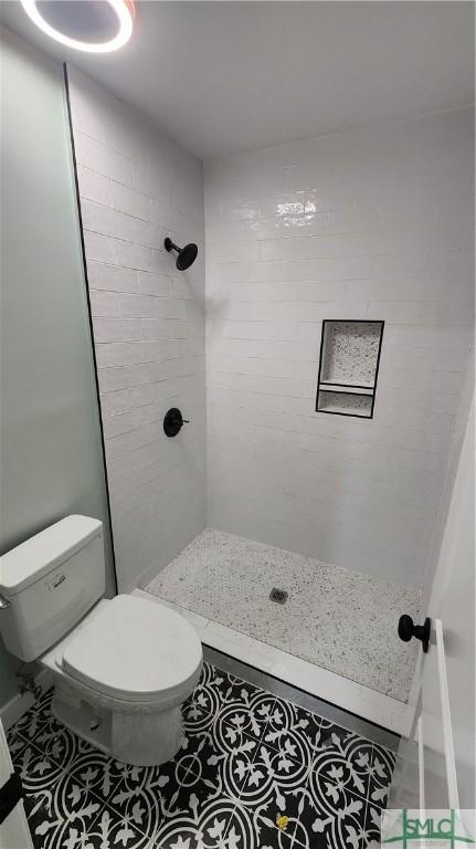 bathroom featuring toilet, tile patterned floors, and tiled shower