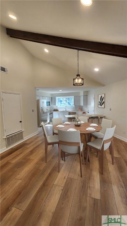 dining area featuring light wood-type flooring, a notable chandelier, and lofted ceiling with beams